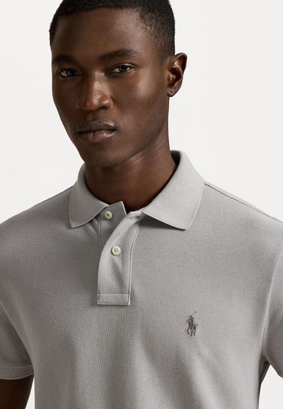 Γκρι πόλο μπλούζα με υφή, τριών κουμπιών, και κεντημένο λογότυπο στο αριστερό στήθος. Κανονική εφαρμογή με κοντά μανίκια.