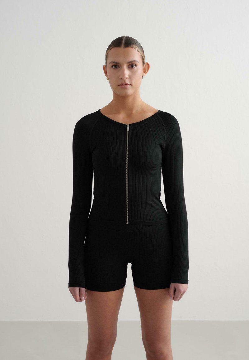 Sort ribbet langærmet lynlåstrøje parret med matchende shorts. Glat tekstur, tætsiddende design og minimalistisk stil uden mønstre eller accenter.