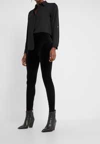 Chemise noire à manches longues, associée à des leggings en velours noir et à des bottines en cuir à bout pointu. Design simple et épuré.