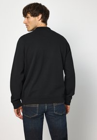 Svart sweatshirt med rund halsringning och långa ärmar, kombinerad med mörkblå jeans. Materialet verkar strukturerat och mjukt. Inga synliga mönster.
