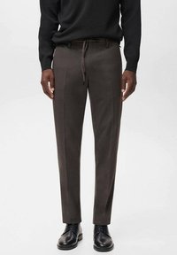 Pantaloni grigi con una texture liscia e una vestibilità slim, dotati di una vita con coulisse e sottili pieghe frontali, abbinati a scarpe nere.
