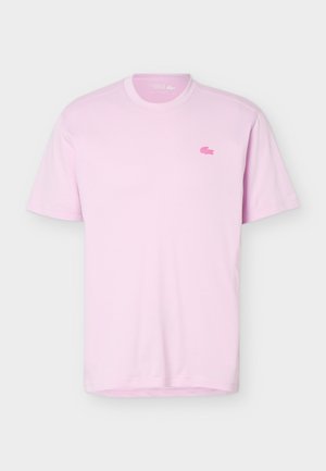 Camiseta de manga corta color rosa claro con cuello redondo y pequeño logo de cocodrilo rosa en el pecho izquierdo.