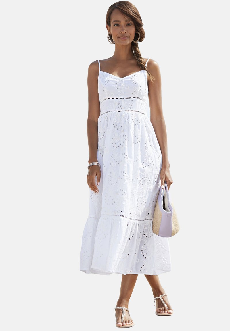 Witte, mouwloze jurk met geborduurde details, een aansluitende lijfje en een uitlopende rok. Gecombineerd met een lavendelkleurige tas en sandalen.