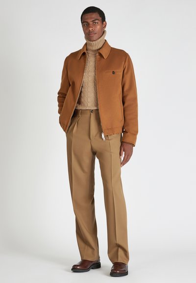 Giacca marrone con zip, dolcevita beige a trama, pantaloni beige e stivali in pelle marrone. Tessuto liscio con dettagli minimi.