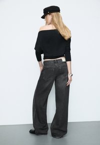 Musta olkaimia ilman paita ja harmaat leveälahkeiset farkut, joissa on takataskut ja kontrastiväriset tikkaus, yhdistettynä mustaan lippikseen ja rannekelloon.