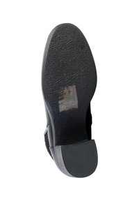Suola di scarpa in gomma nera con superficie testurizzata, motivo di battistrada prominente e adesivo istruttivo chiaro visibile sul lato inferiore.