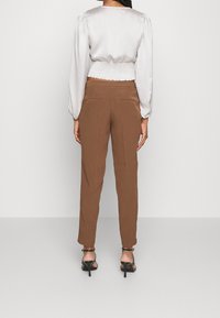 Brązowe, dopasowane spodnie o gładkiej fakturze, zestawione z jasnoszarą satynową bluzką z bufkami i marszczoną talią.