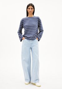 Marineblaues langärmliges gestreiftes Hemd, hellblaue weite Jeans und weiße Sneakers; entspannte Passform mit abgesenkten Schultern und seitlichen Taschen.