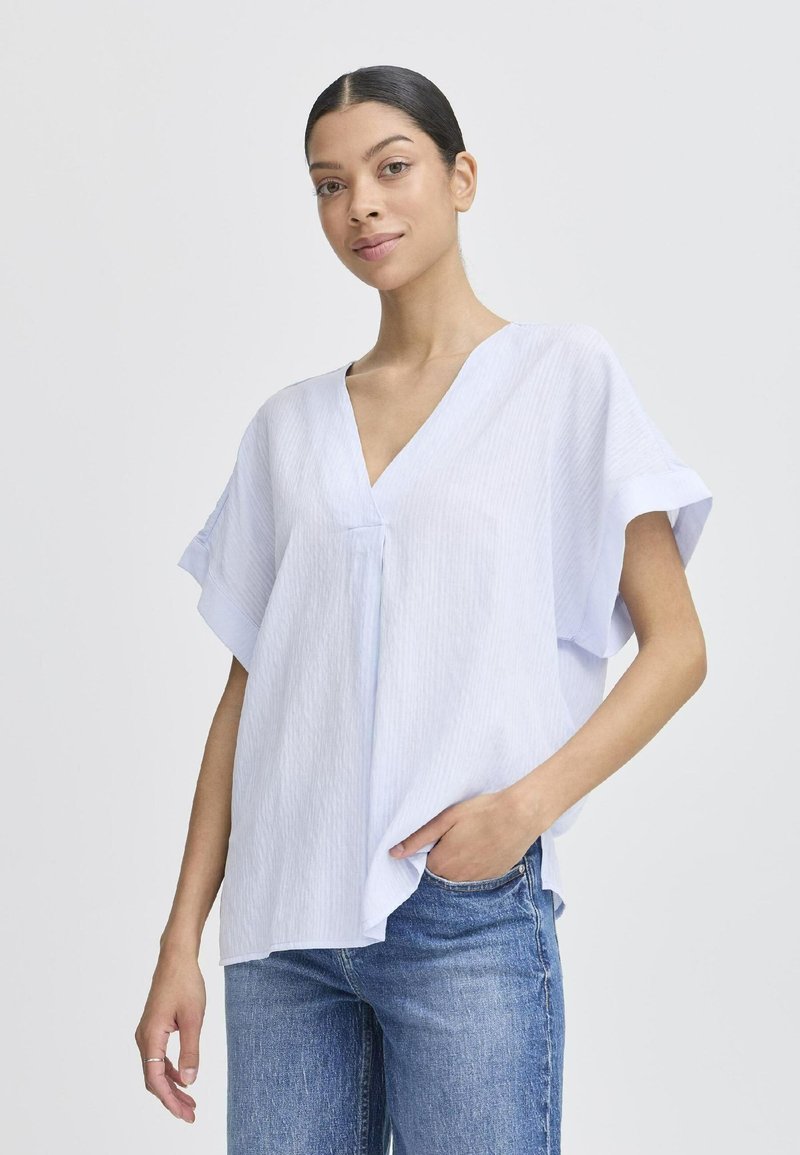 Blusa a righe blu chiaro con scollo a V e maniche corte. Realizzata in un tessuto morbido e leggero. Abbinata a jeans blu.