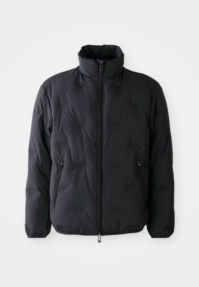 Casaco acolchoado preto com um colarinho alto, fecho de correr frontal completo e dois bolsos laterais. Apresenta uma textura suave e um detalhe de marca discreto.