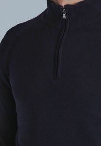 Marineblauer Pullover mit einem halben Reißverschluss am Kragen, geripptem Halsausschnitt und glatter Textur. Figurbetontes Design mit minimalen Nähdetails.