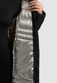 Čierny vonkajší materiál so lesklou, metalicky striebornou podšívkou. Polstrovaný dizajn s prešívanou textúrou a viditeľnou kapsou na vnútornej vrstve.