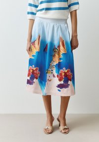 Een vloeiende lichtblauwe rok met een levendige print van kliffen, een kleurrijk gebouw en bloemaccenten aan de zoom. Gemaakt van een zachte stof.