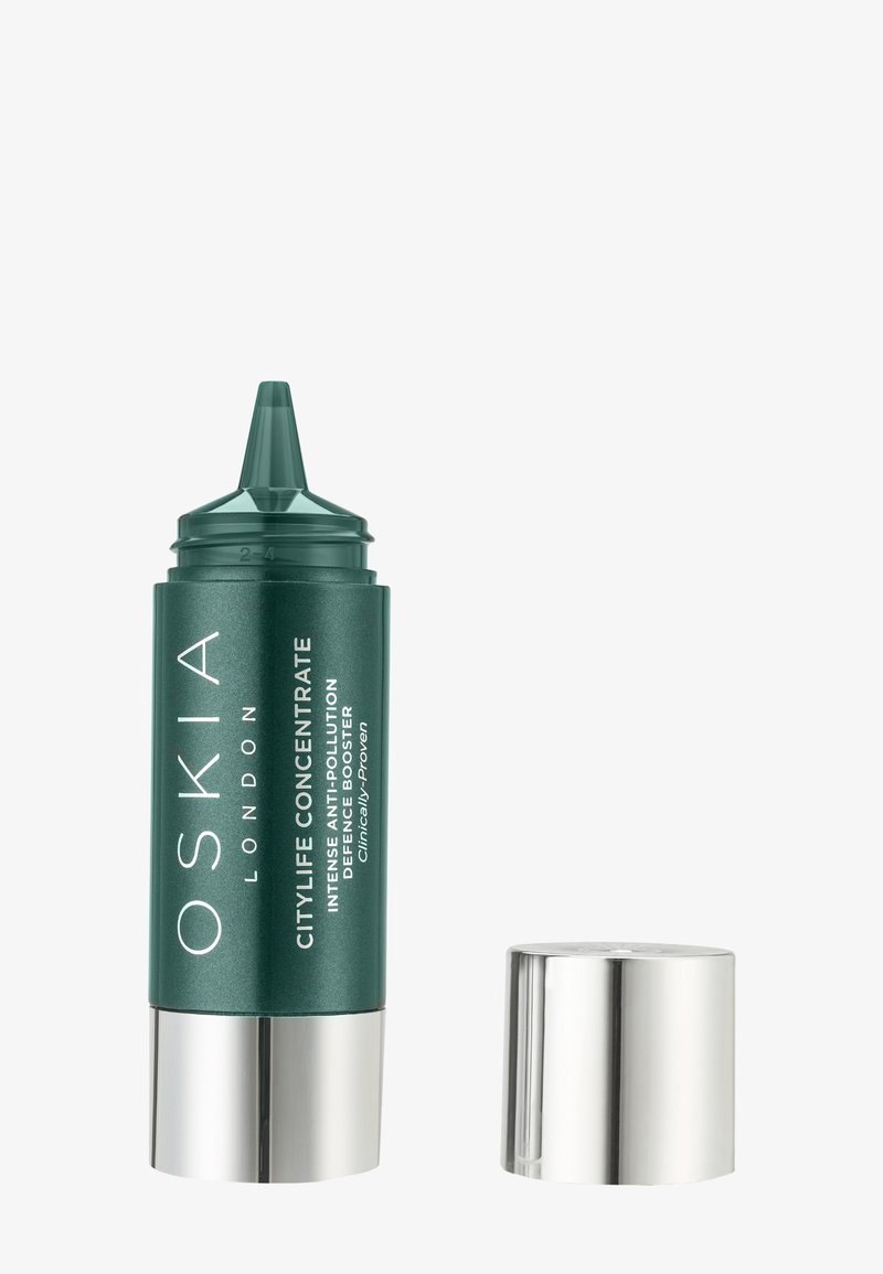 Bouteille de soin pour la peau cylindrique verte avec un embout effilé. Base et capuchon en argent. L'étiquette présente un texte blanc détaillant le nom du produit et ses avantages.