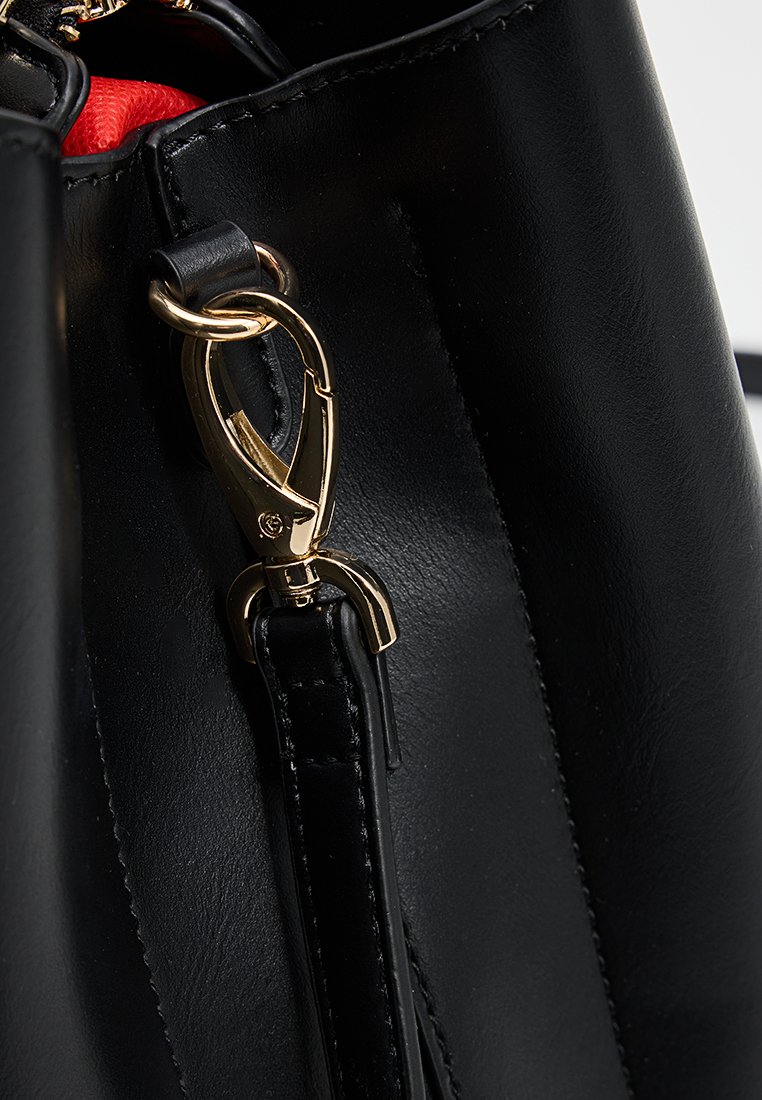 Dettaglio di una borsa in pelle nera con una chiusura in metallo dorato e una texture liscia, con un rivestimento rosso nascosto visibile all'interno.