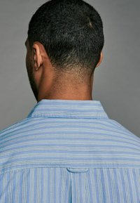 Light blue striped shirt featuring a classic collar, a yoke design on the back, and a subtle pocket detail.