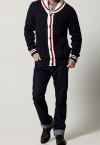 Marinblå stickad cardigan med vit och röd sjalkrage, försedd med träknappar; matchad med mörka jeans och svarta ankelstövlar.