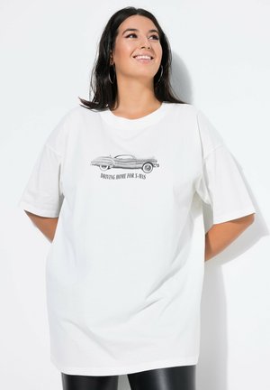 Vit oversized t-shirt med en svart bilgrafik och texten "DRIVER HEM FÖR JUL". Korta ärmar, rund halsringning och mjukt tyg.