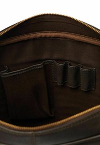 Det mørkebrune læderbags indre har en glat tekstur, med en kontrasterende lyse stofforing og flere lommer til organisation.