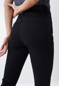 Jeans de mezclilla negra con un diseño ajustado, que cuentan con dos bolsillos traseros con sutiles detalles de costura y una textura suave.