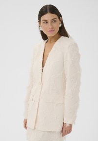 Šviesiai rožinė ilgos rankovės švarkas iš tekstūruoto audinio, su suplėšytais akcentais, V formos iškirpte, dviem priekinėmis kišenėmis ir viena mygtuko uždarymo.