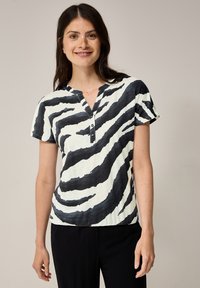 Korte mouwen, V-hals top in licht crème met zwarte zebraprinten, met een knopenlijst en een ontspannen pasvorm. Zachte, gestructureerde stof.
