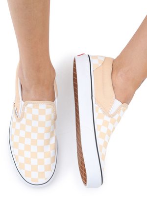 Slip-on sneakers med et beige og hvitt rutete mønster, myk tekstiloverdel, elastiske sideakenter og en strukturerte gummisåle.