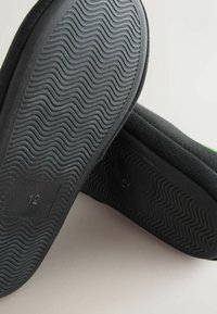 Black footwear with a textured rubber sole featuring a wave pattern. Size "12" marked on the side, with a soft upper material.