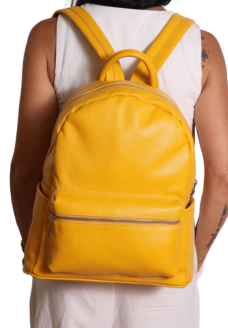 Zaino giallo in pelle con superficie testurizzata, forma arrotondata, spallacci regolabili e tasca frontale con zip.
