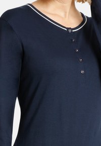 Navy long-sleeve top with a scoop neckline, featuring a white trim, five button closure, and soft, smooth fabric texture.