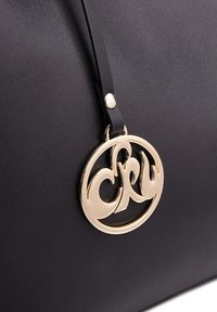 Sort læderhåndtaske med et goldmetal logo mærke med et rundt design og bogstaverne "CRY," fastgjort med en sort rem.