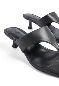 Zwarte leren haksandalen met een gebogen voorband en open teen. Beschikken over een kleine, vierkante hak en gestikte details langs de randen.