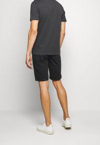 Pantalones cortos de mezclilla negros y una camiseta gris oscuro. El atuendo se completa con zapatillas blancas. Detalle de costura sutil en la camiseta y los pantalones cortos.