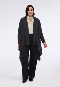 Cardigan grigio ardesia con una texture a coste, apertura frontale e orlo asimmetrico, abbinato a una blusa beige e pantaloni scuri.