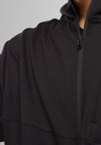 Sudadera con cremallera negra que presenta un cuello alto, textura suave y detalles de costura en el cuerpo para un diseño minimalista.