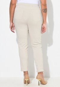 Pantaloni beige slim-fit con superficie testurizzata, vita elastica e due tasche posteriori. Abbinati a tacchi alti nudi con dettagli dorati.