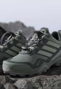 Jasnozielone buty trekkingowe mają teksturowaną syntetyczną cholewkę, szare akcenty, smukły design oraz system szybkiego sznurowania dla pewnego dopasowania.