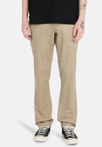 Beige cotton pants with a straight cut, featuring side pockets and a smooth texture, paired with black canvas sneakers.