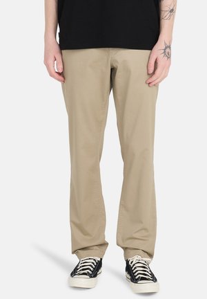 Beige cotton pants with a straight cut, featuring side pockets and a smooth texture, paired with black canvas sneakers.
