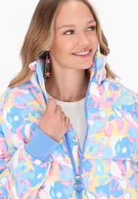 Polstrovaná bunda s vícebarevným abstraktním vzorem v modré, růžové a žluté, s vysokým límcem a žebrovanými manžetami. Klíčový úchyt ve tvaru srdce.