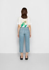 T-shirt branca de manga curta com uma gráfica floral colorida nas costas, combinada com jeans retos de cintura alta azul clara e sandálias pretas.