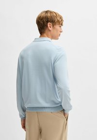 Ljusblå, långärmad pikétröja med ribbad krage och kant. Slät textur, minimalistisk design och diskret sömdetaljering.