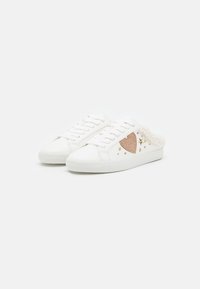 Weiße Sneaker mit strukturiertem Design, herzförmigem Detail und metallischen Akzenten. Schnürverschluss und weiche Fütterung im Rücken.