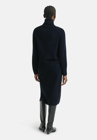 Navy turtleneck dress in a soft texture, with a relaxed fit, knee-length cut, and ribbed detailing at the collar, paired with sleek black boots.