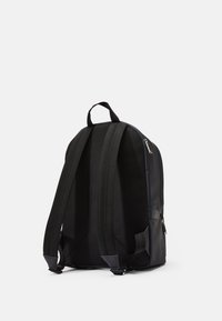 Mochila negra con un acabado mate, correas de tela acolchadas y un respaldo texturizado. Presenta un cierre de cremallera y un diseño elegante.