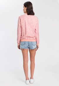 Różowa bluza z kwiatowym wzorem, z prążkowanymi mankietami i dołem, w połączeniu z dżinsowymi szortami o postrzępionych brzegach i luźnym kroju.