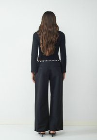 Zwart aansluitend shirt met lange mouwen, gecombineerd met losse zwarte wijde broek. De tailleband heeft decoratieve zilveren hardware accenten.