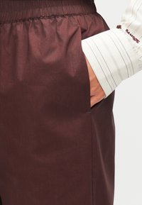 Pantalon léger bordeaux avec une taille élastique et des poches latérales. Présente une texture lisse et un léger éclat.