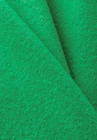 Gros plan d’un tissu vert doux et duveteux avec un motif en maille texturé et des plis qui se chevauchent.