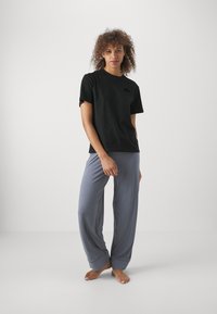 Melna kokvilnas T-kreklu ar īsām piedurknēm un mazu logotipu, kombinēts ar brīvām, gaismas pelēkām, mīkstām biksēm ar salocītām malām.